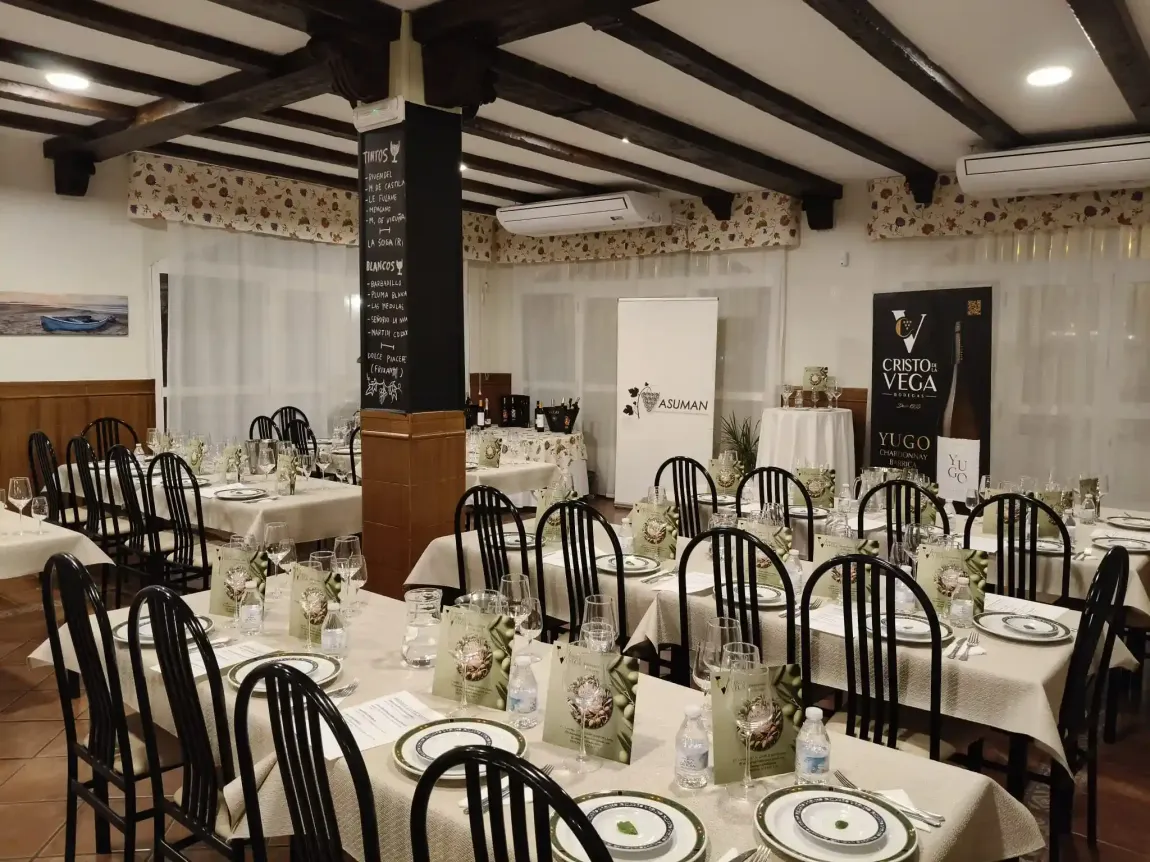 Interior de restaurante con mesas preparadas para comer. El salón luce un techo rústico con vigas oscuras.
