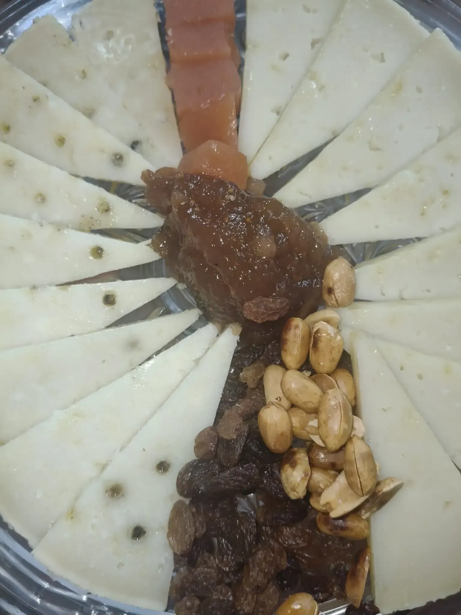 Tabla de quesos y acompañamientos: lonchas de queso, mermelada oscura, pasas, cacahuetes y otra mermelada.