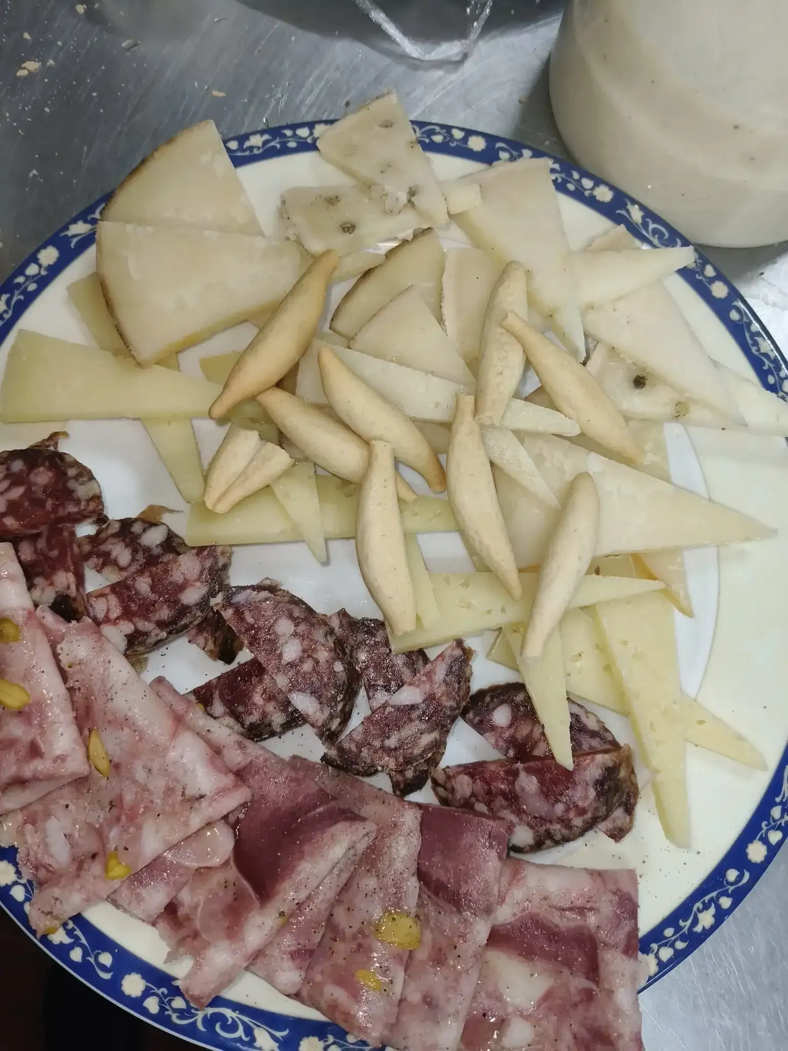 Plato de quesos variados en lonchas, embutidos y palitos de pan.