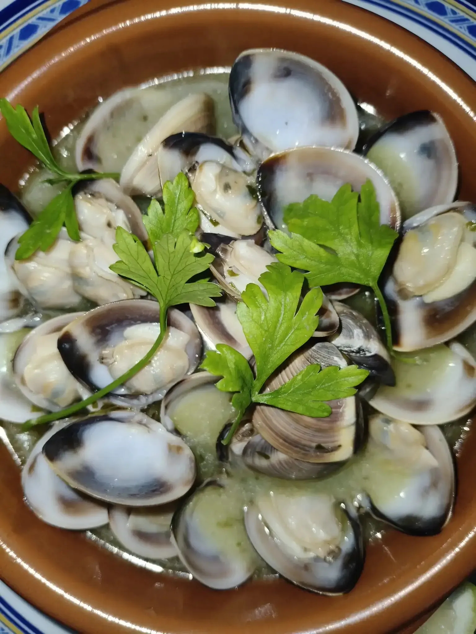 Almejas en salsa cremosa, adornadas con perejil, servidas en un recipiente de cerámica.