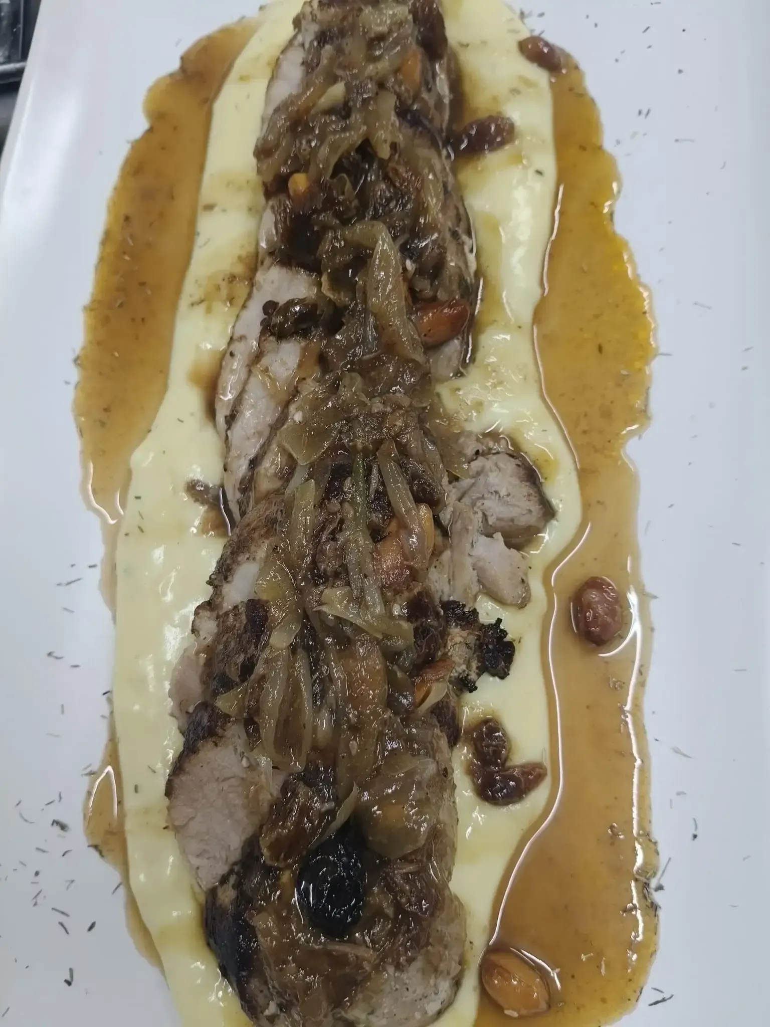 Solomillo de cerdo en rodajas con cebollas caramelizadas, salsa y puré de patatas en un plato blanco.