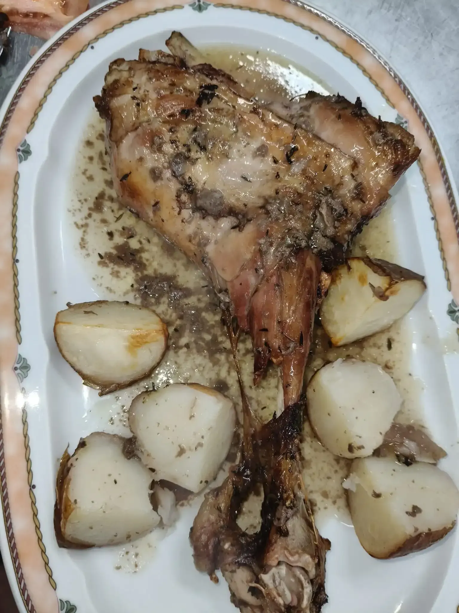 Muslo de conejo asado y patatas en bandeja de servir con salsa.
