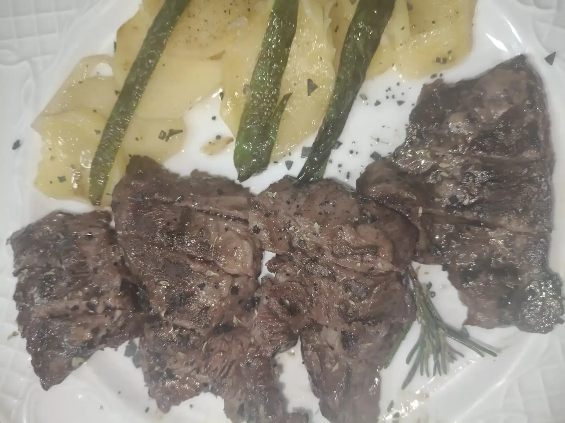 Bistec a la parrilla, patatas y judías verdes en un plato blanco; condimentado con pimienta y sal.