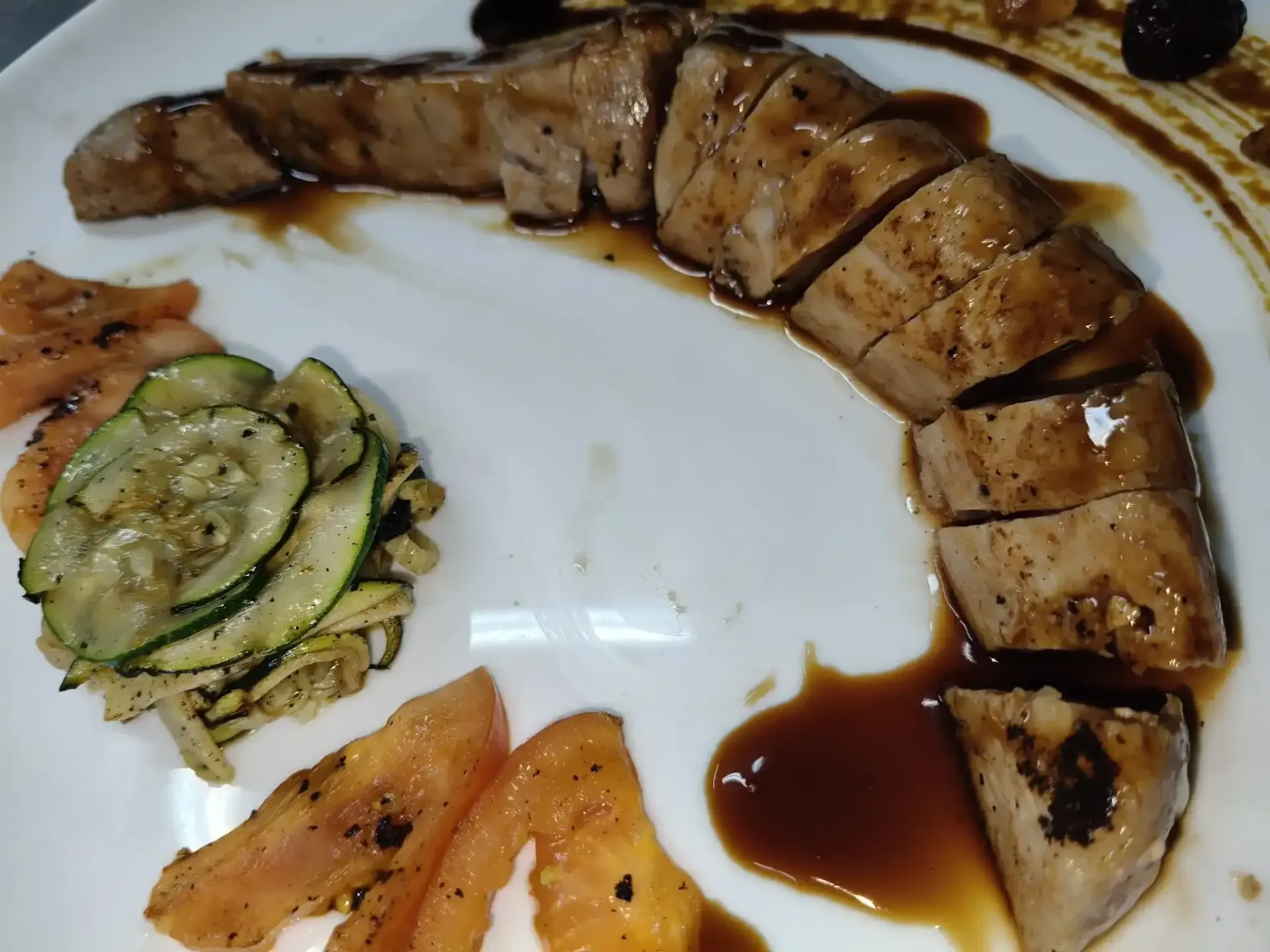 Carne cocida en rodajas con salsa, calabacín y tomate en un plato blanco.