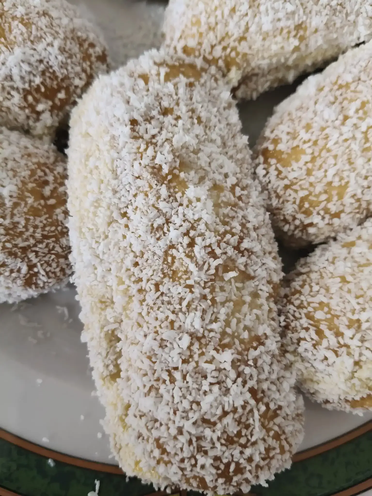 Primer plano de rollitos de hojaldre dorados cubiertos con coco rallado, apilados en un plato blanco.