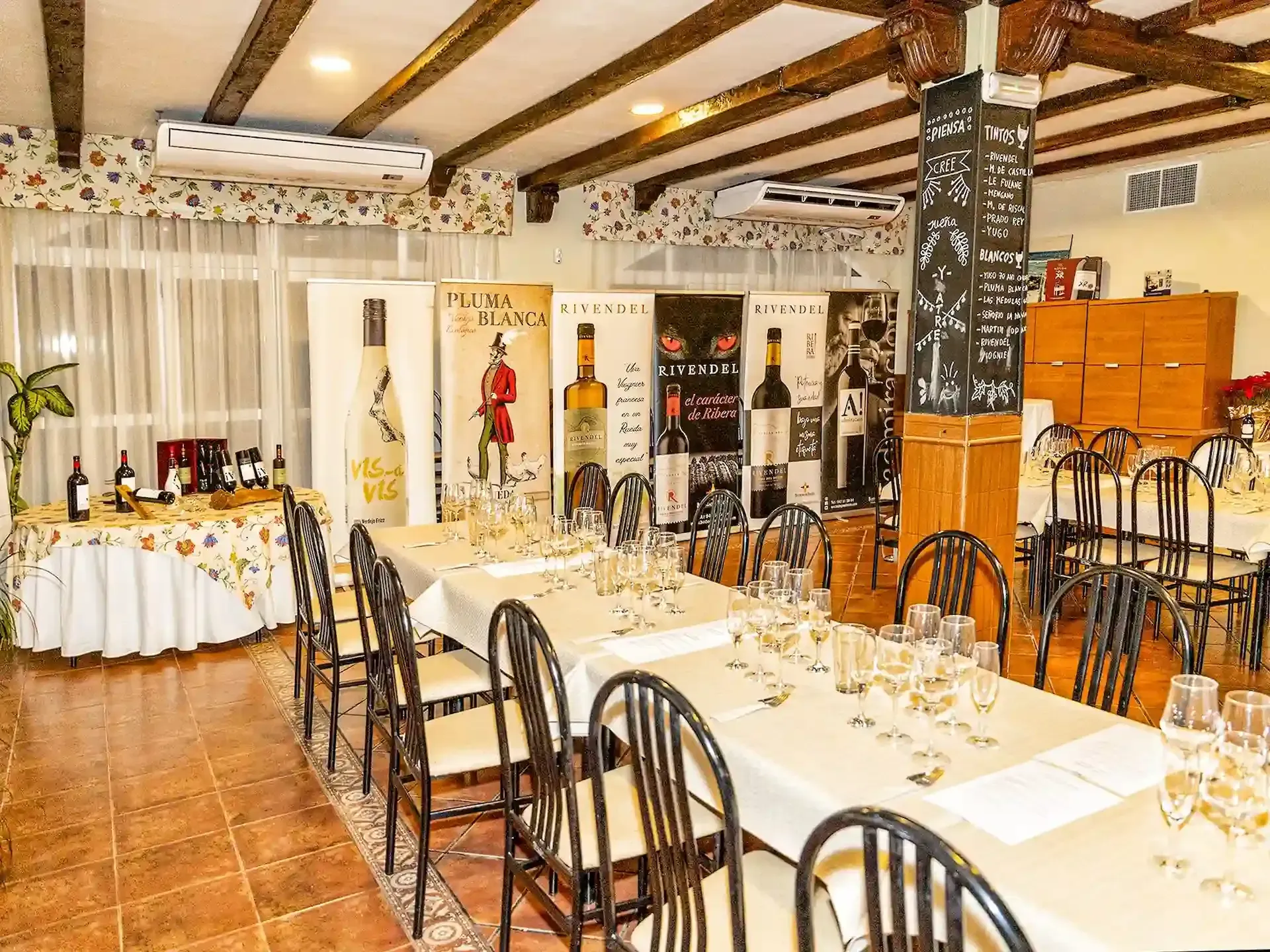 Evento de cata de vinos: mesas largas dispuestas con copas, carteles promocionales y botellas en un lugar interior.