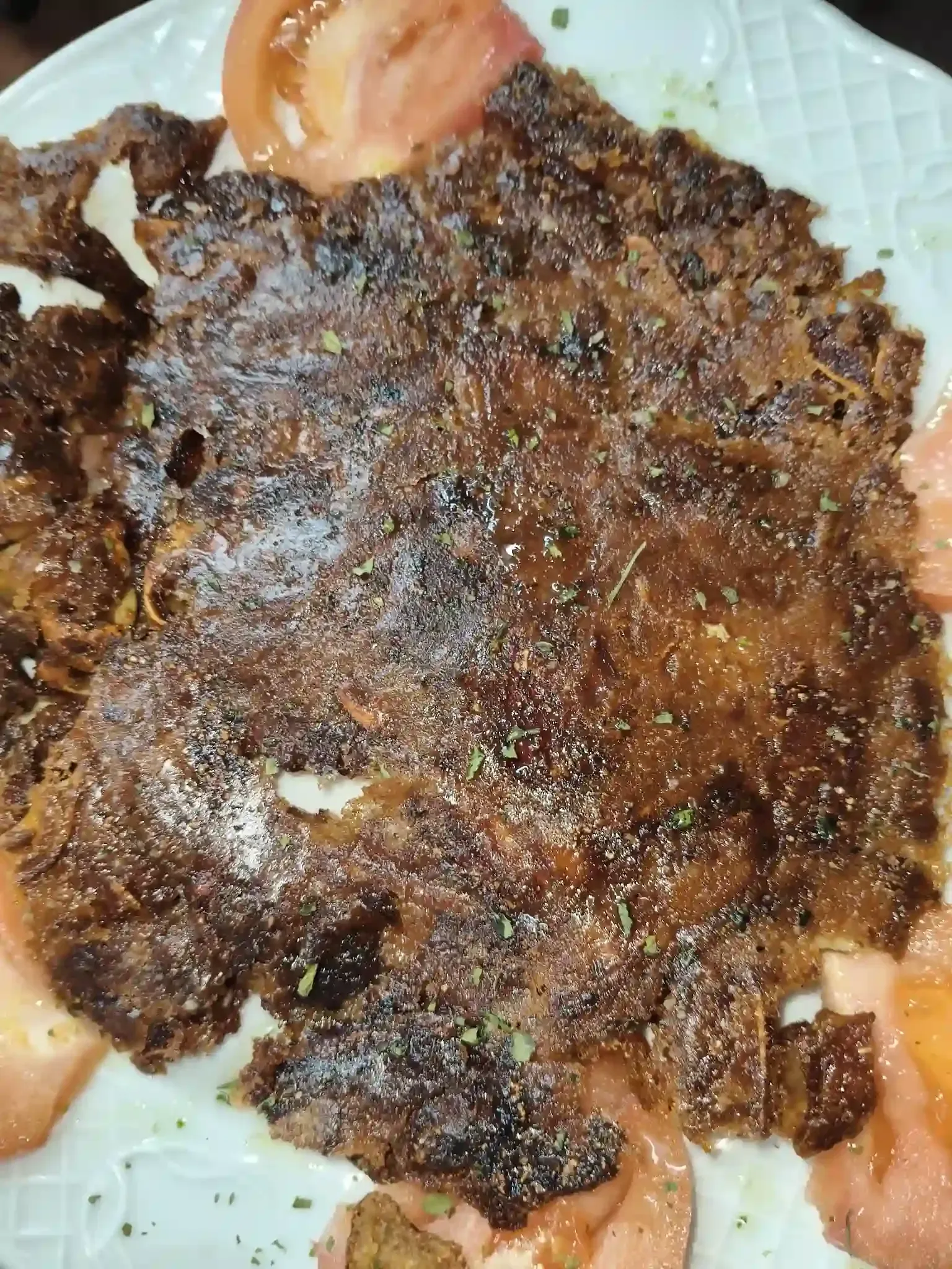 Comida marrón y crujiente en un plato blanco con rodajas de tomate.