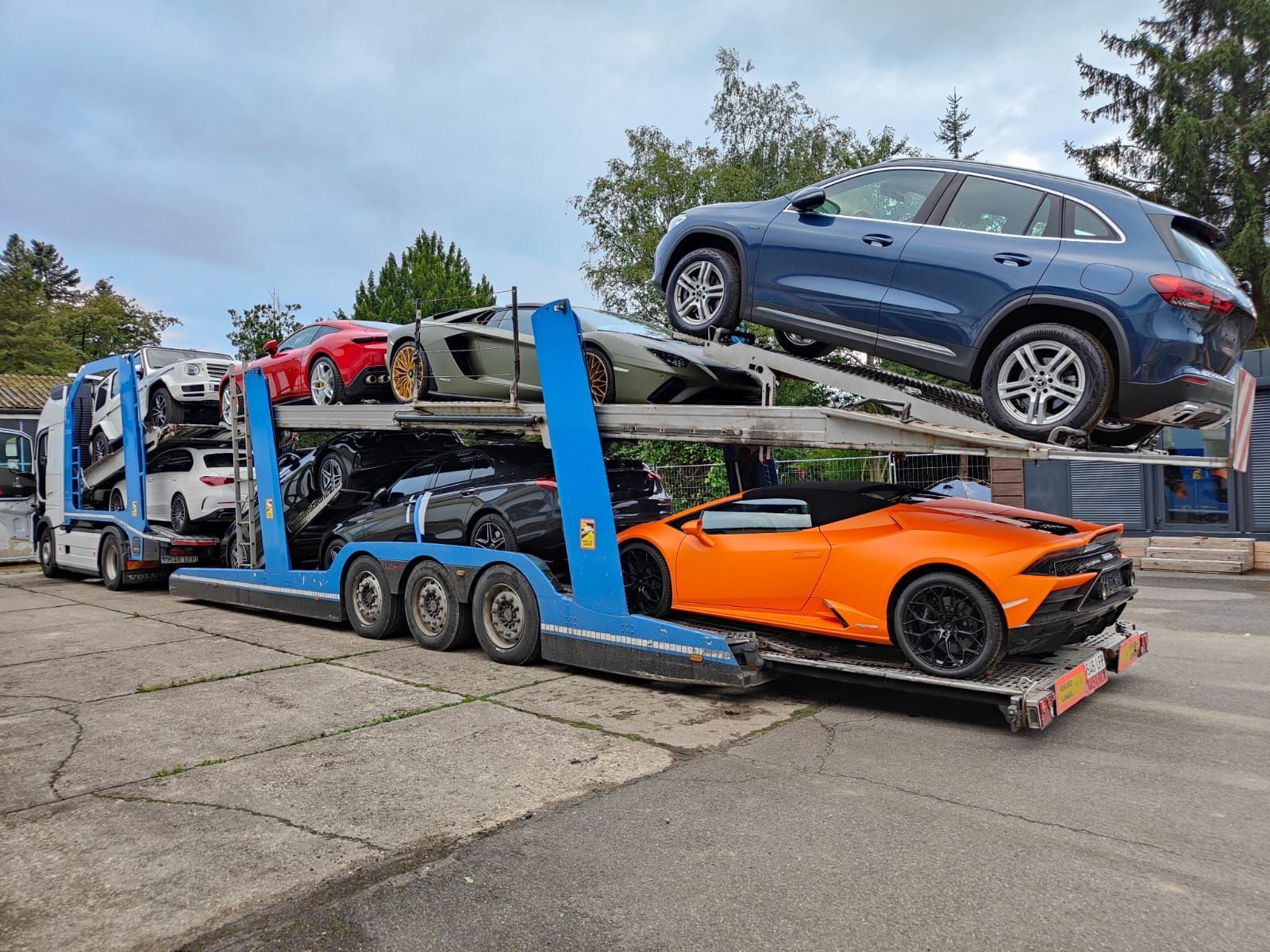 Camión transportador de automóviles cargado con varios coches deportivos y todoterrenos de colores sobre una superficie de hormigón.