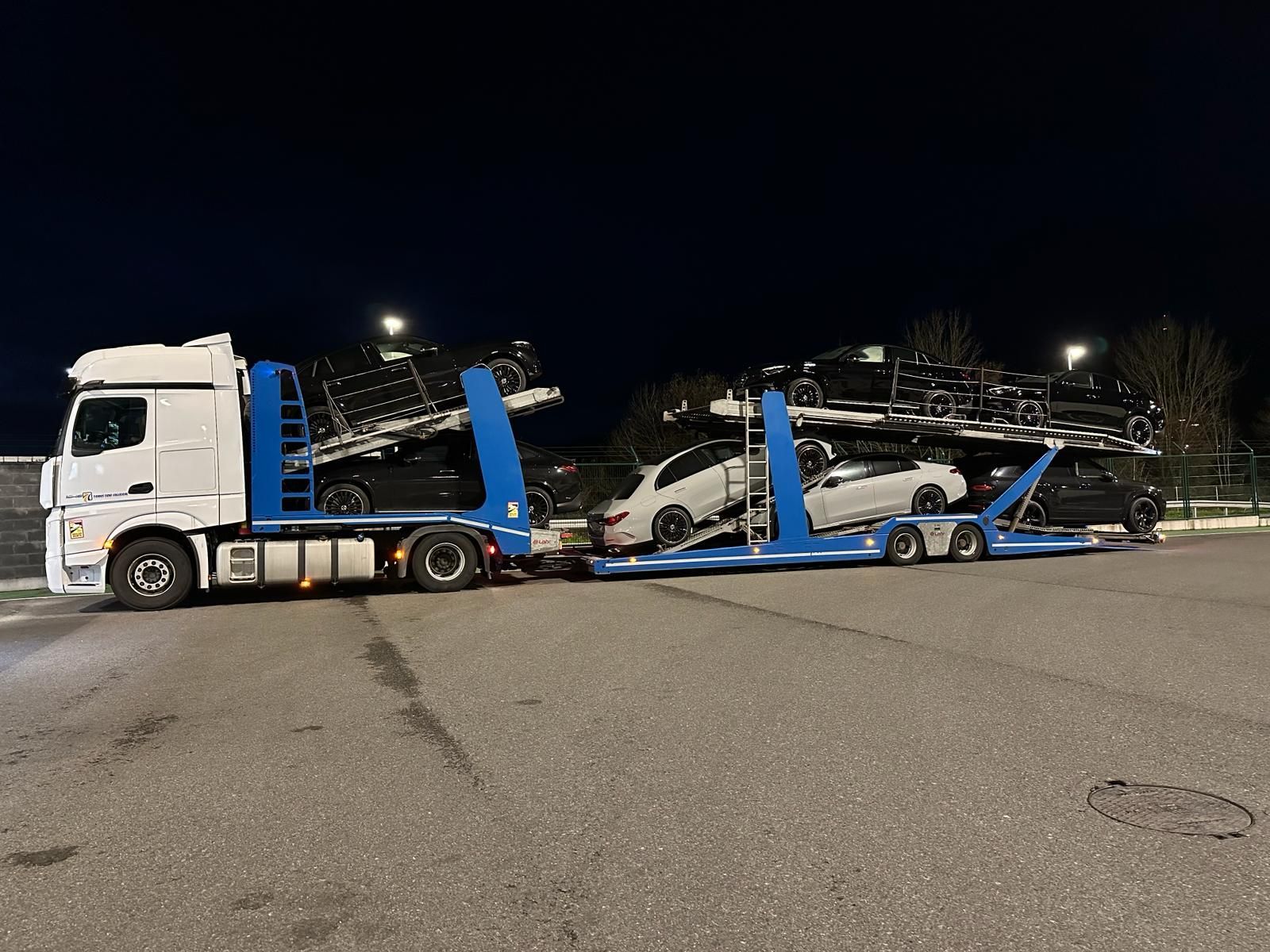 Camión portacoches cargado con vehículos estacionados al aire libre por la noche.