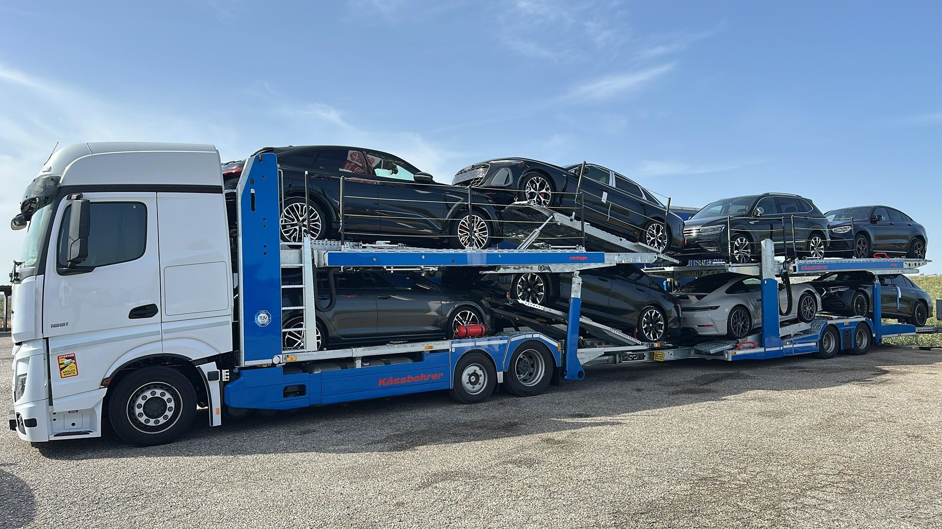 Un camión transportador de automóviles que transporta varios coches deportivos blancos y negros en un día soleado.