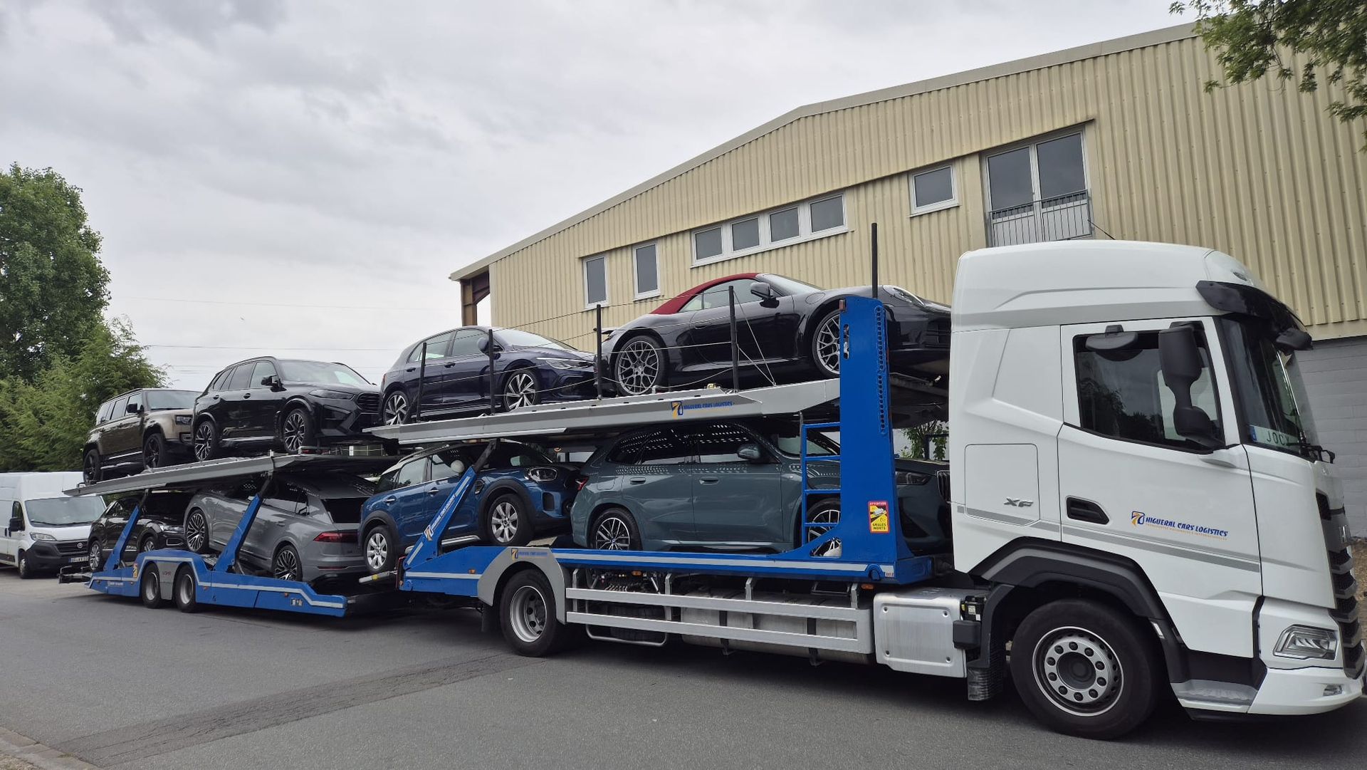 Camión transportador de automóviles transportando varios vehículos; al aire libre, cielo nublado.