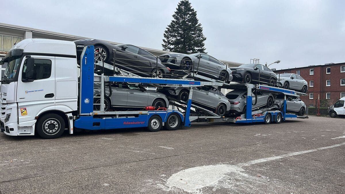 Camión portacoches que transporta varios coches deportivos grises en un aparcamiento asfaltado.