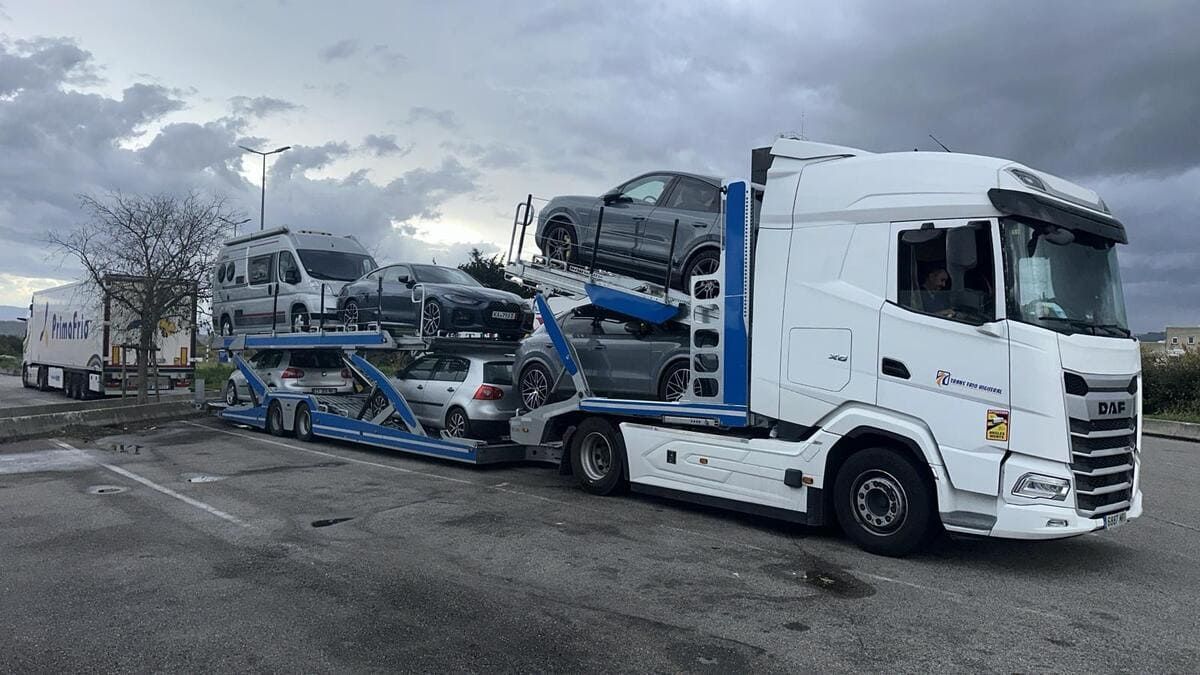 Un camión portacoches blanco transportando varios vehículos en un día nublado.