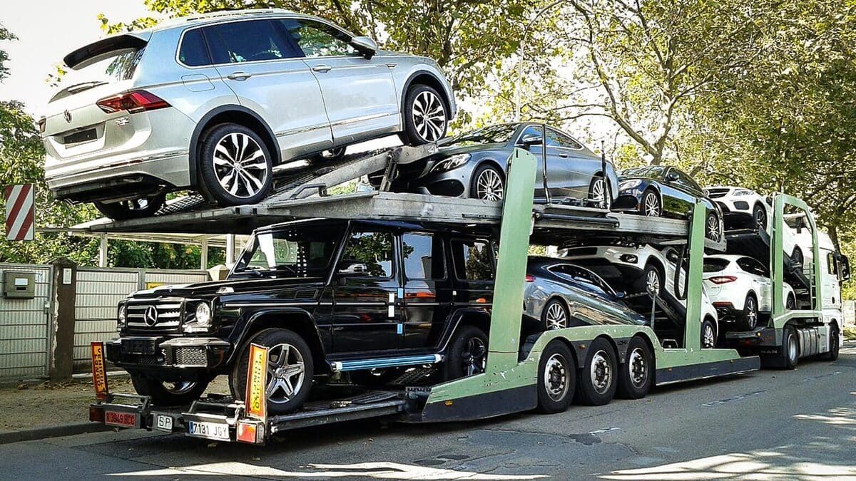 Camión portacoches cargado con varios vehículos, estacionado en una carretera.