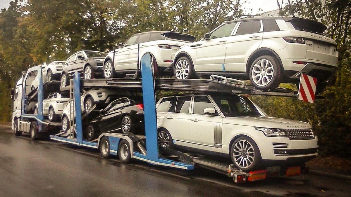 Un camión portacoches cargado con varios todoterrenos blancos y negros estacionado en una carretera.