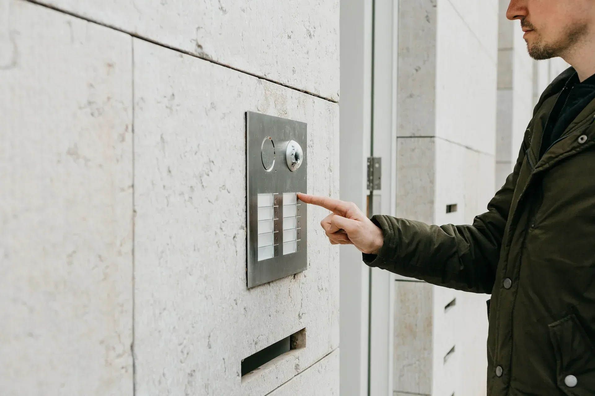 Persona presionando un botón de timbre en un panel de metal colocado en una pared de piedra.