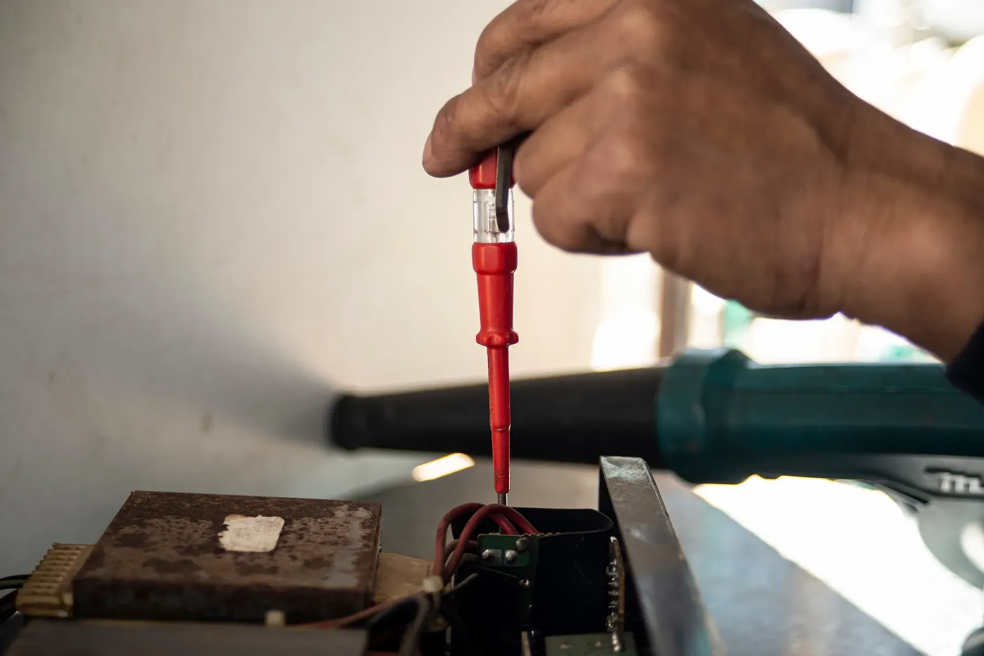 Persona que utiliza un comprobador de voltaje rojo en cables eléctricos dentro de un dispositivo.