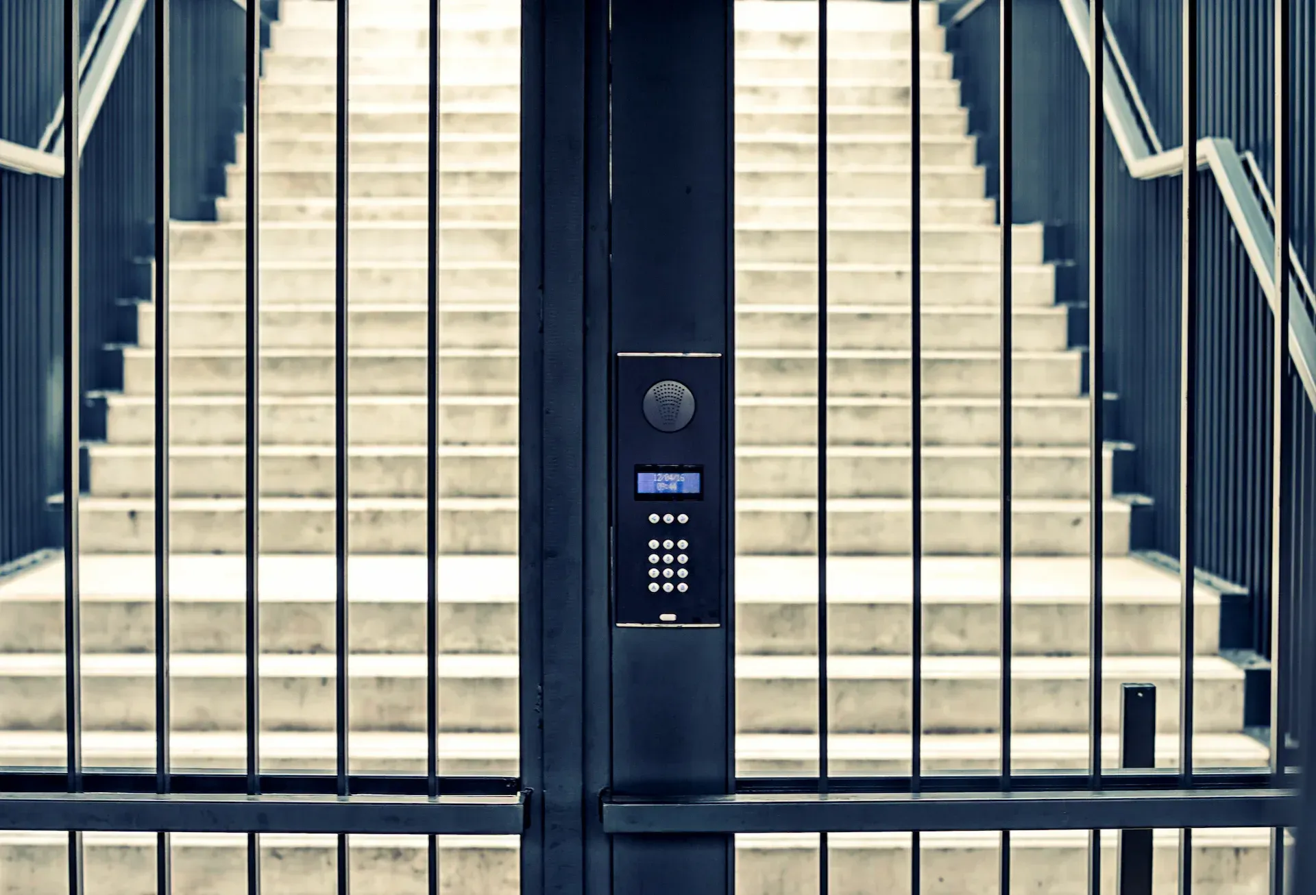 Puerta de metal negro con teclado que conduce a una escalera de hormigón simétrica.