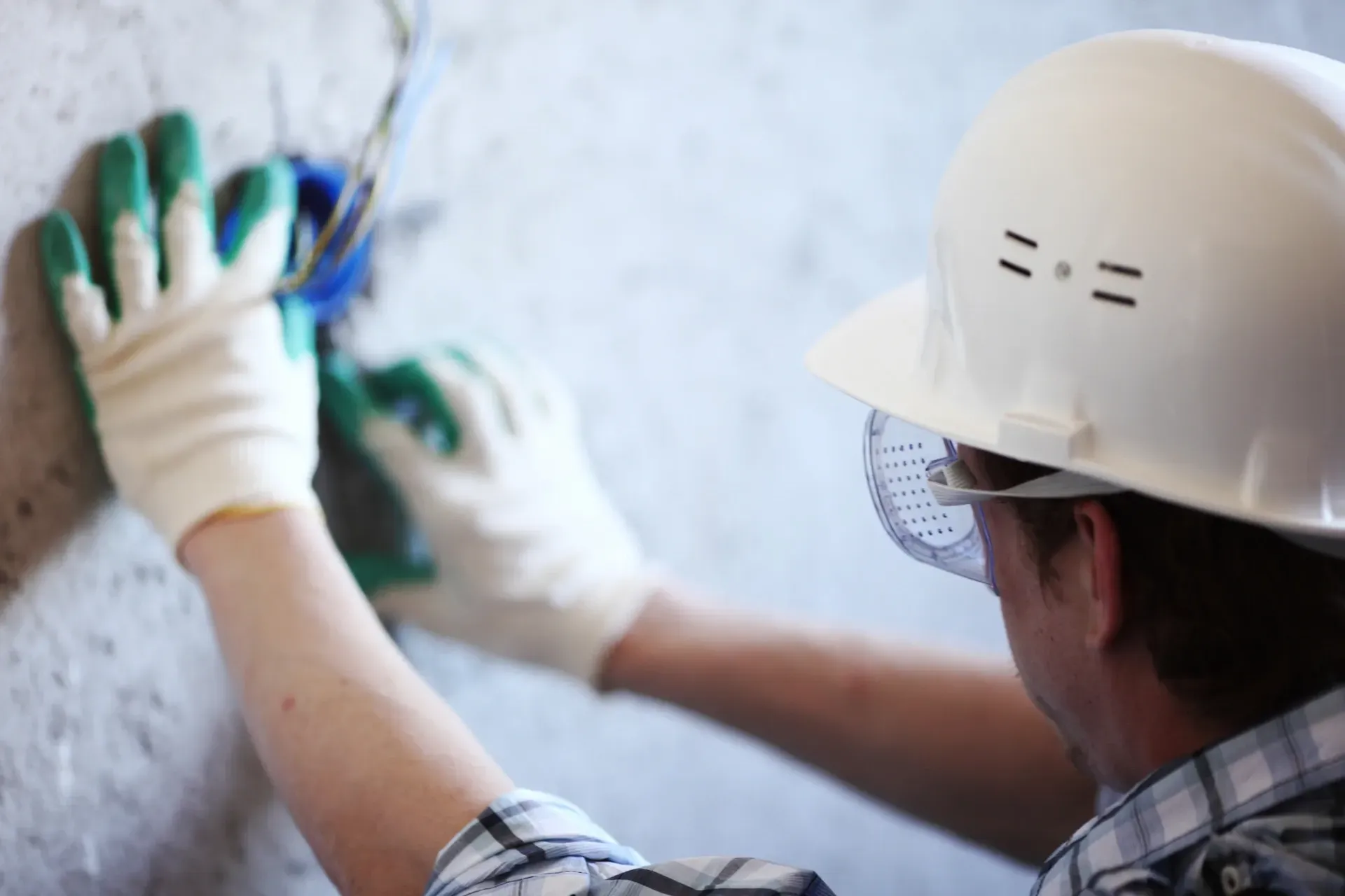 Trabajador con casco y guantes instalando cableado en una pared.