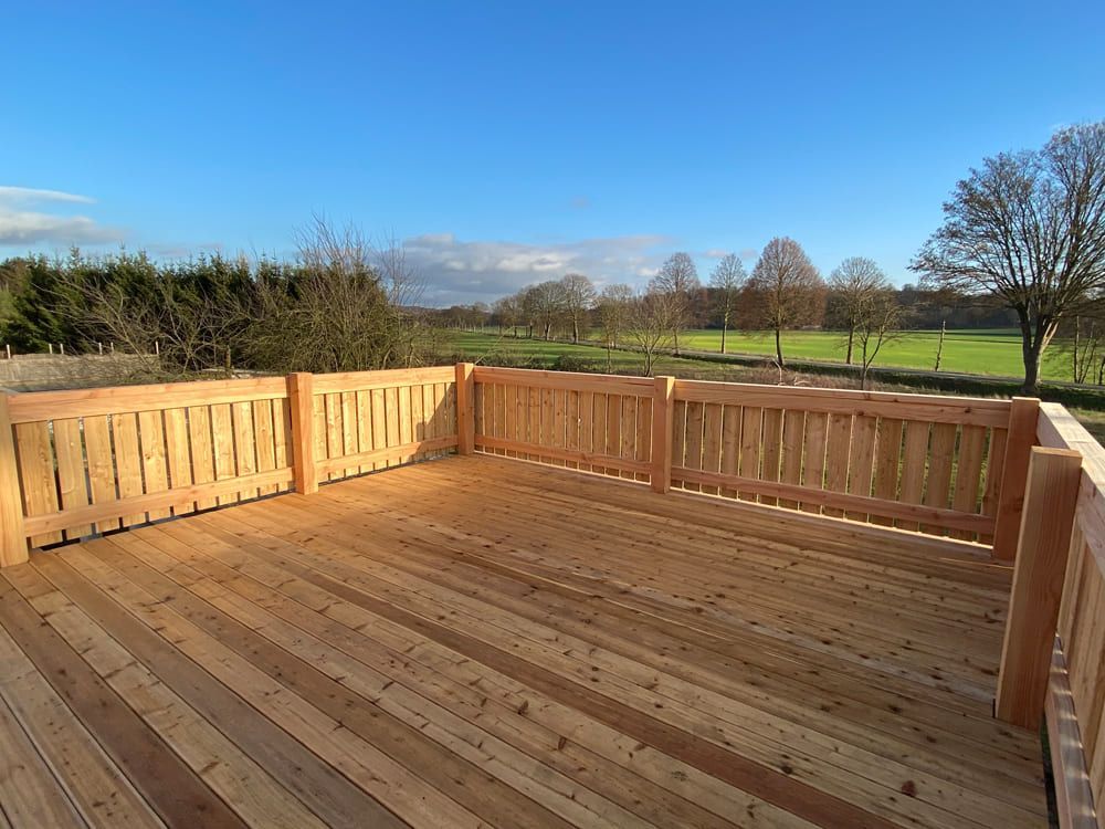 Eine Holzterrasse mit Zaun und Blick auf ein Feld.