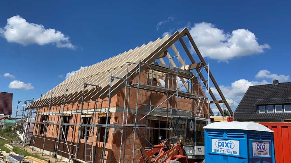 Es wird ein Haus mit Gerüst gebaut, davor steht eine blaue Mobiltoilette.