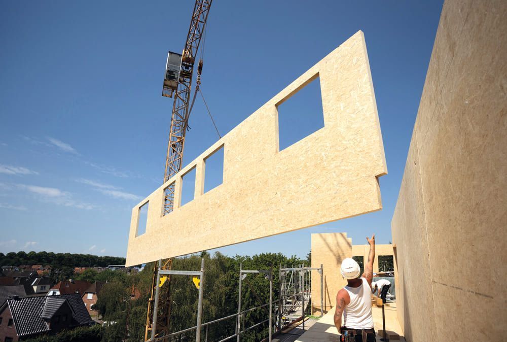 Ein Bauarbeiter hebt ein Stück Holz auf ein Gebäude.
