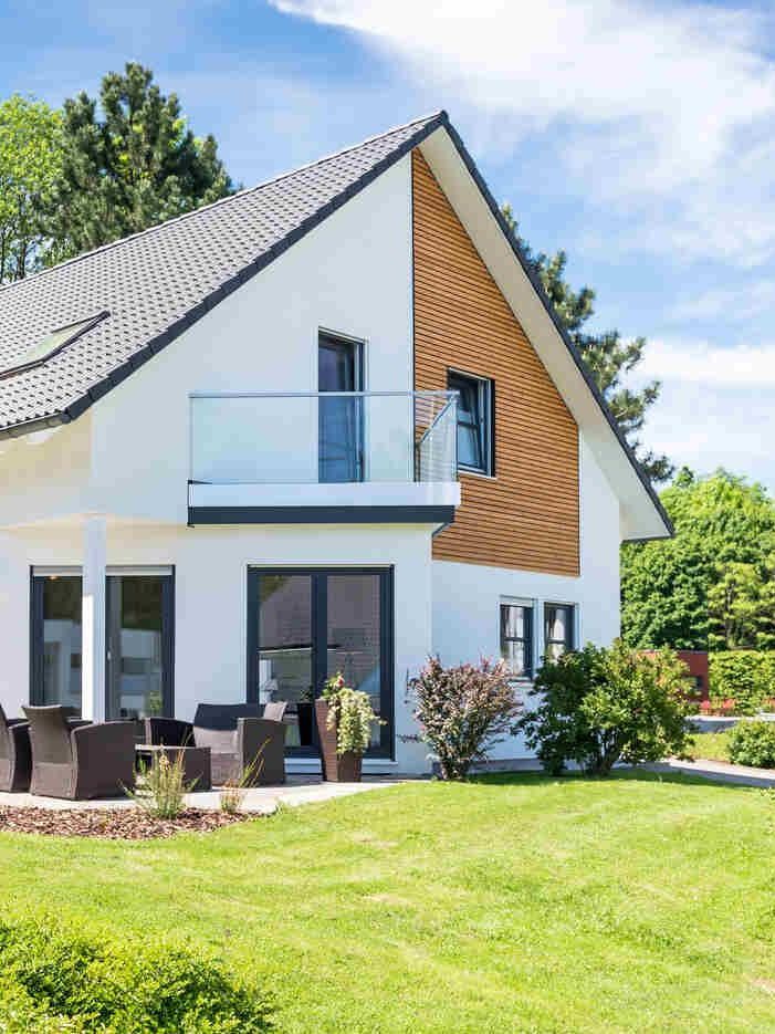 Ein weißes Haus mit Balkon und großer Wiese davor.
