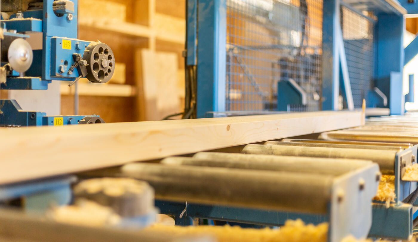 In einer Fabrik schneidet eine Maschine ein Stück Holz.