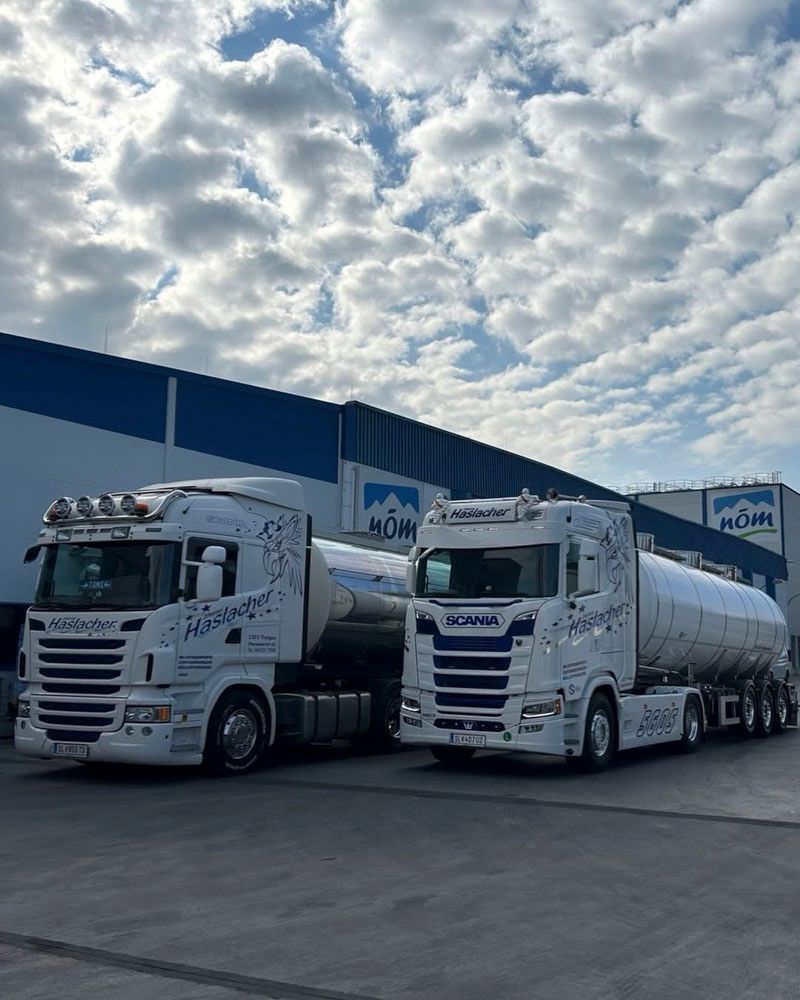Zwei weiße Scania-Tankwagen parkten nebeneinander vor einem blau-weißen Industriegebäude unter bewölktem Himmel.