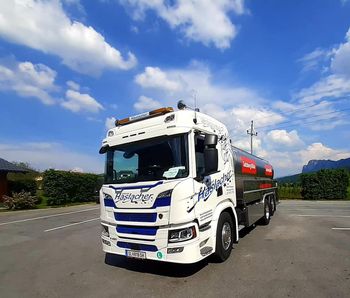Ein weißer Tankwagen mit blauen Akzenten parkt unter einem teilweise bewölkten Himmel.