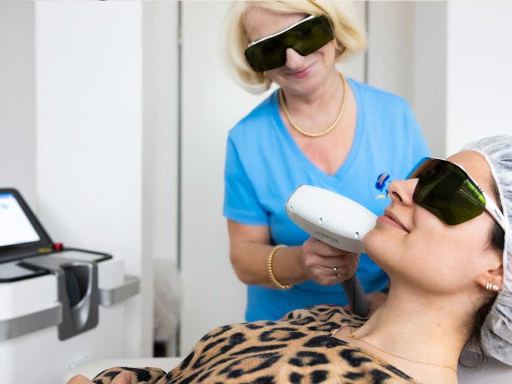 Eine Frau im blauen Oberteil führt eine Gesichtsbehandlung bei einer im Behandlungsstuhl sitzenden Dame durch