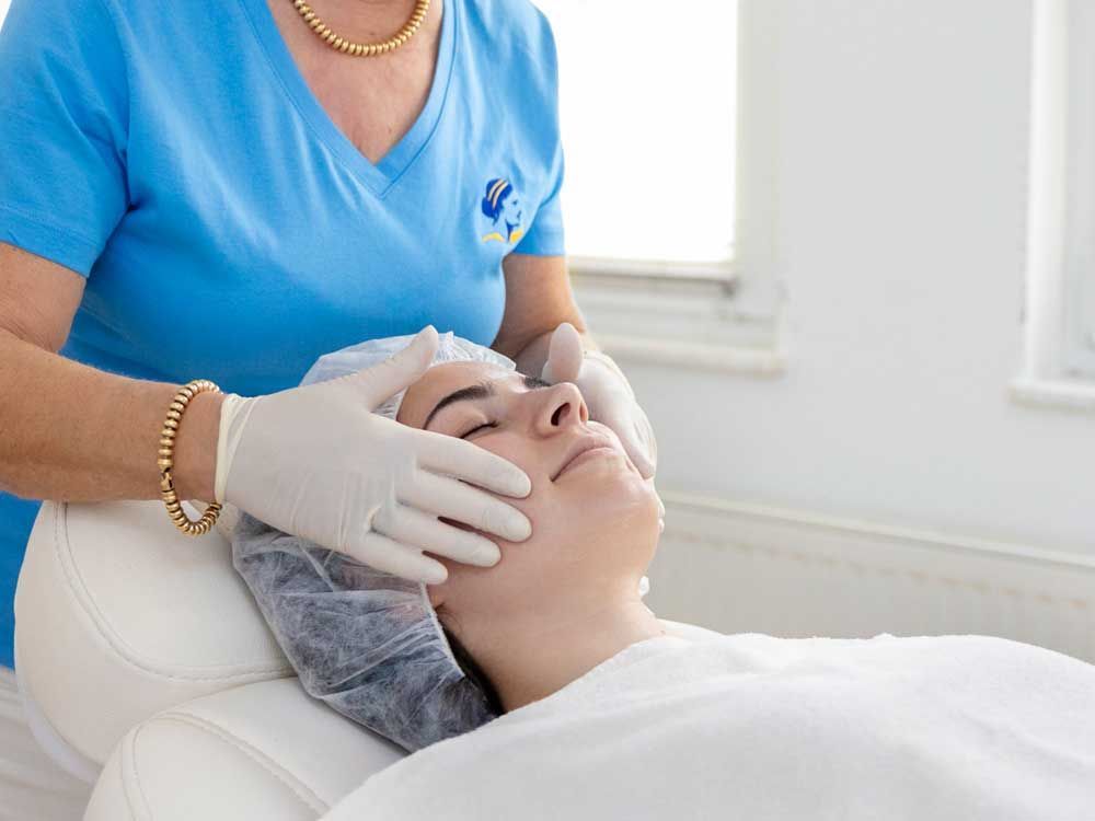 Eine Frau im blauen Oberteil führt bei einer Frau eine Gesichtsbehandlung durch