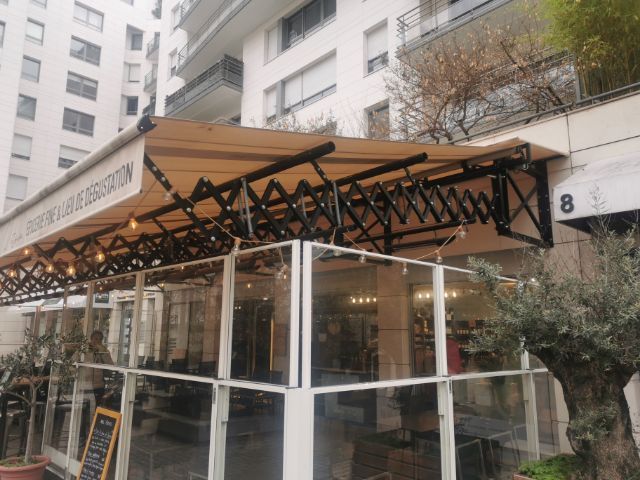 Un store pantographe au-dessus d'une terrasse fermée.