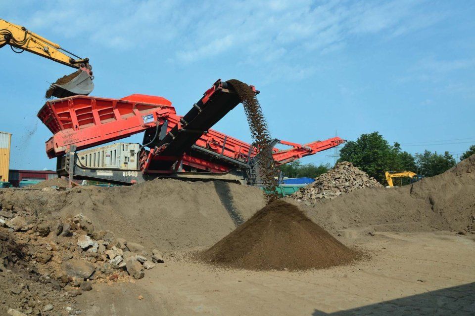 Gelber Schaufelbagger belädt roten Verteiler, der Erde auf einen Haufen gießt