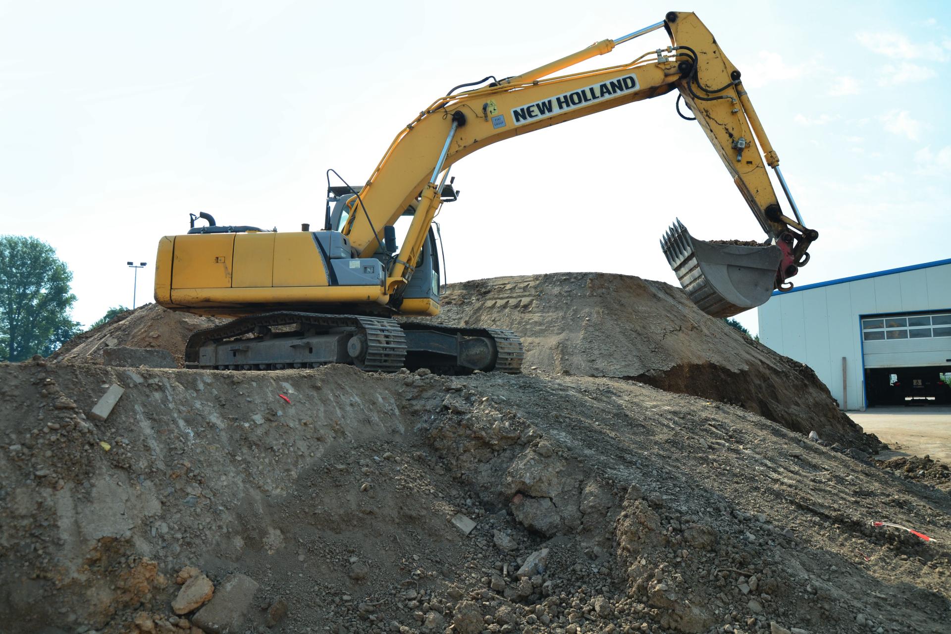 Gelber Bagger baggert auf einem großen Haufen Bauerde