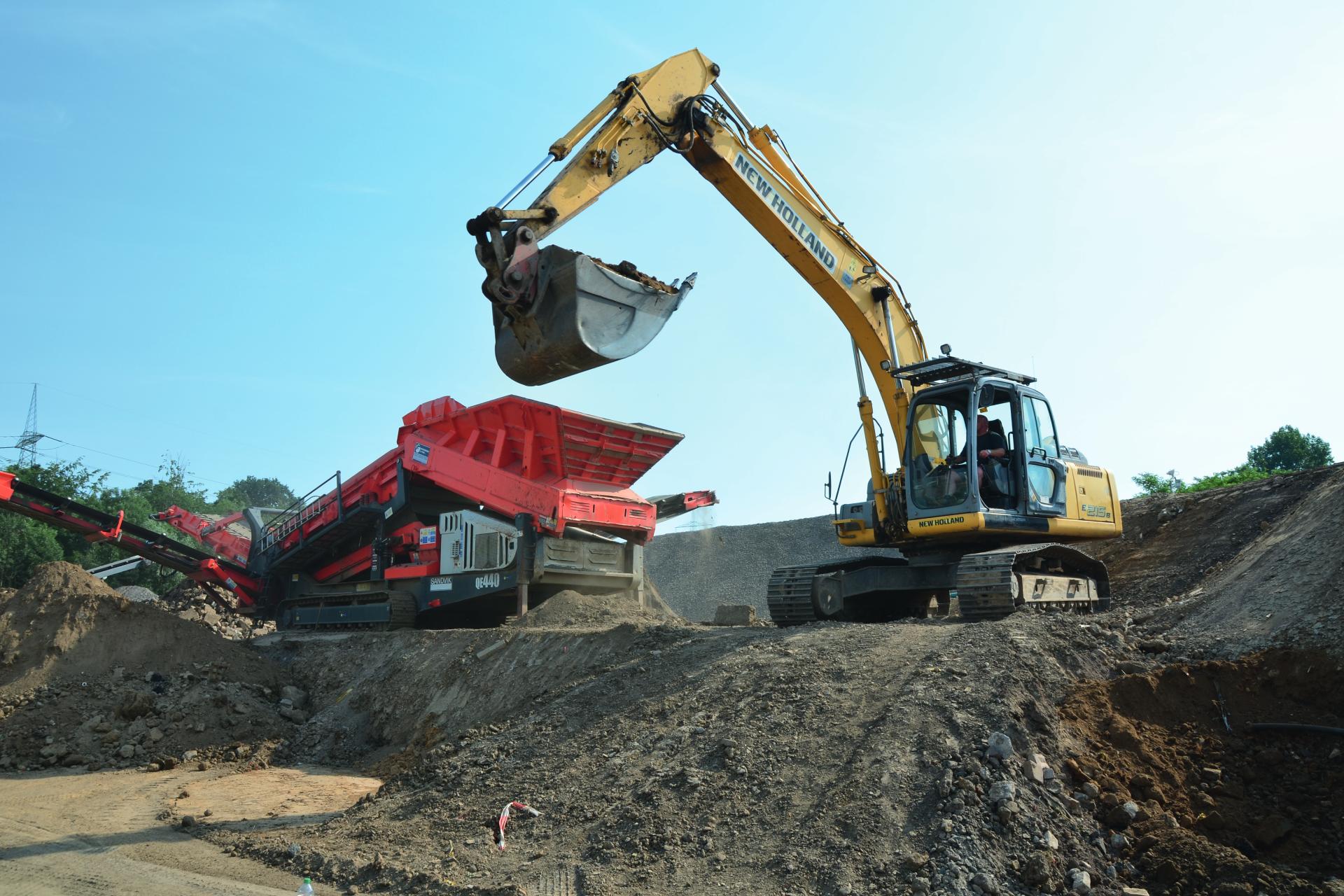 Gelber Bagger belädt Verteilermaschine mit Schutt