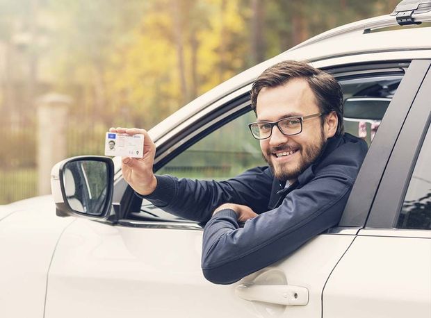 Un hombre está sentado en un automóvil sosteniendo una licencia de conducir.