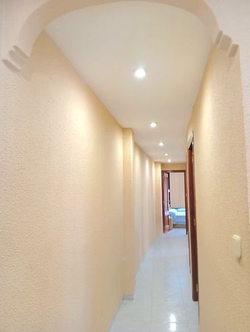 Pasillo estrecho de color beige con luces empotradas en el techo y una puerta abierta al final.