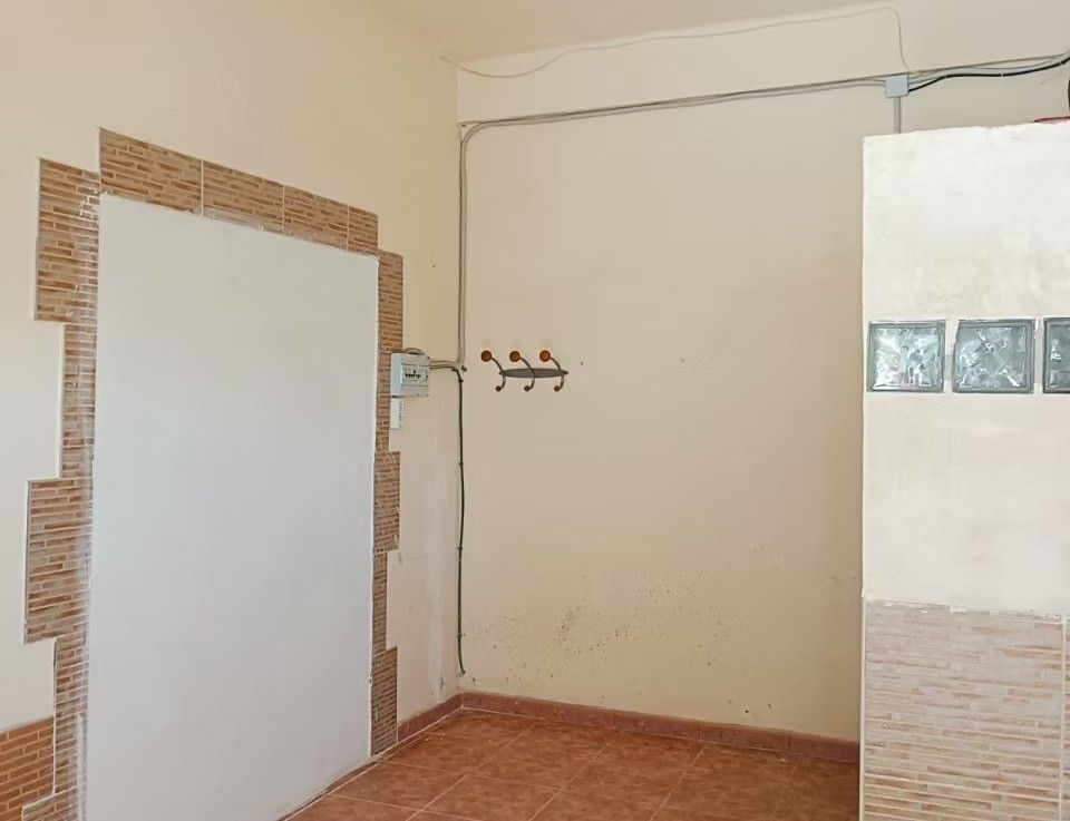 Habitación vacía con azulejos, puerta blanca, percheros en la pared y una pequeña ventana de bloques de vidrio.