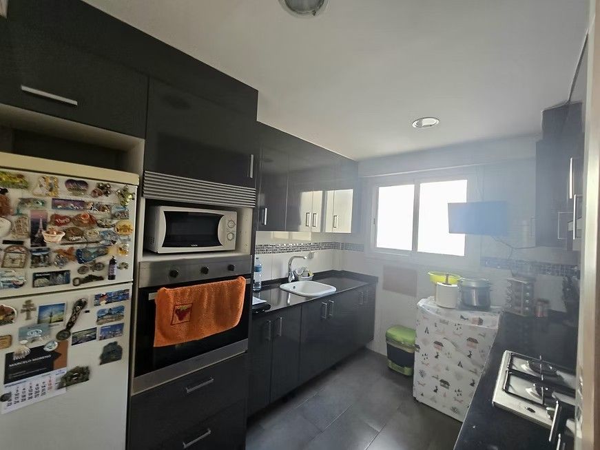 Cocina moderna en blanco y negro con microondas, fregadero, refrigerador y luz natural proveniente de la ventana.