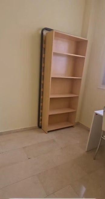 Estantería de madera vacía contra una pared beige en una habitación sin adornos con suelo de baldosas.
