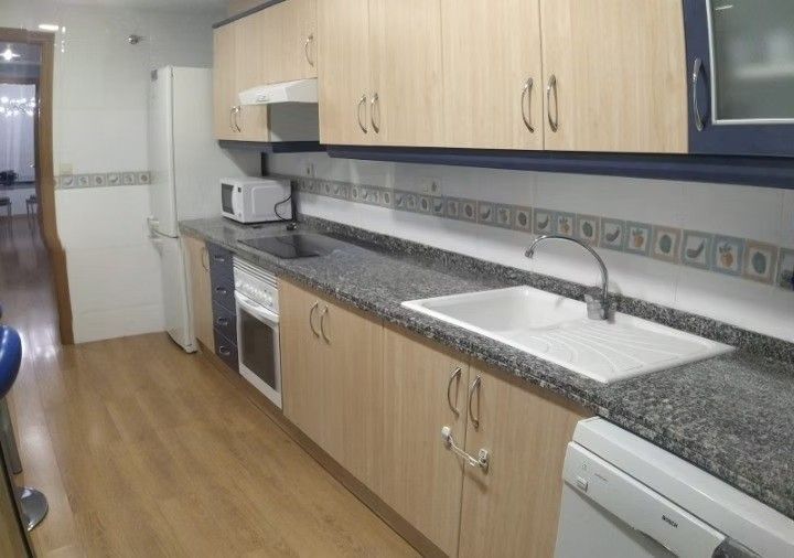 Cocina moderna y estrecha con armarios de madera clara, encimeras de granito, fregadero, cocina y electrodomésticos blancos.