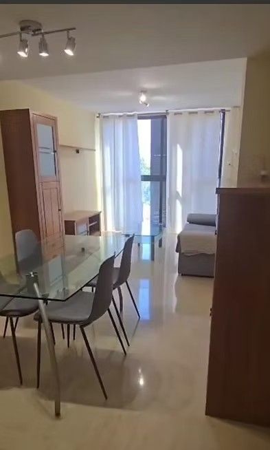 Luminoso salón-comedor con mesa de cristal, sillas, sofá y puertas correderas que dan a un balcón.