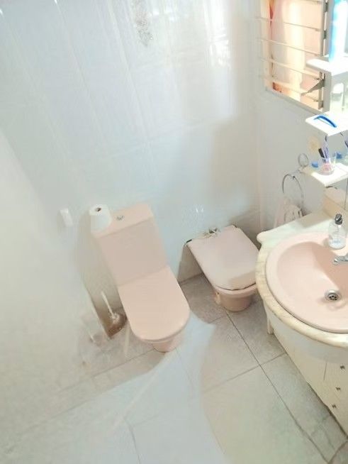 Baño pequeño de color blanco con inodoro, bidé, lavabo y suelo de baldosas cerca de una ventana.
