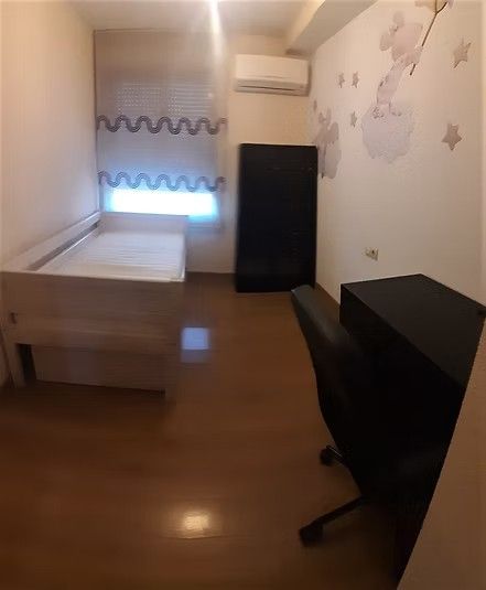 Habitación pequeña con cama, escritorio, silla negra y aire acondicionado de pared.