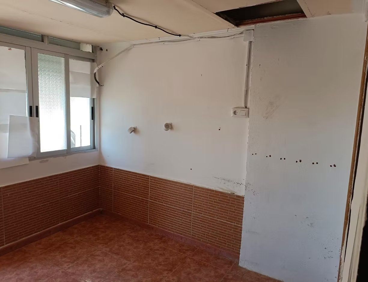 Habitación vacía con paredes blancas, revestimiento inferior de ladrillo, una ventana y suelo de baldosas.