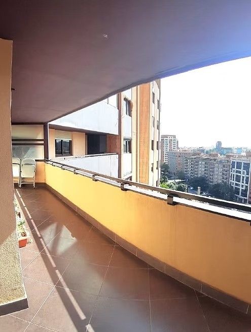 Balcón cubierto de un apartamento con barandilla naranja con vistas a los edificios de la ciudad al atardecer.