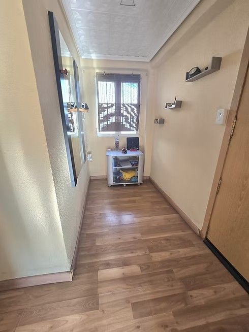 Pasillo estrecho con suelo de madera, paredes de color beige, ventana al final y un pequeño carrito de almacenamiento.