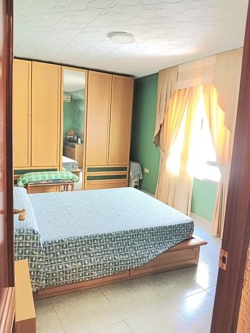Habitación pequeña con cama, armario y ventana luminosa con cortinas.