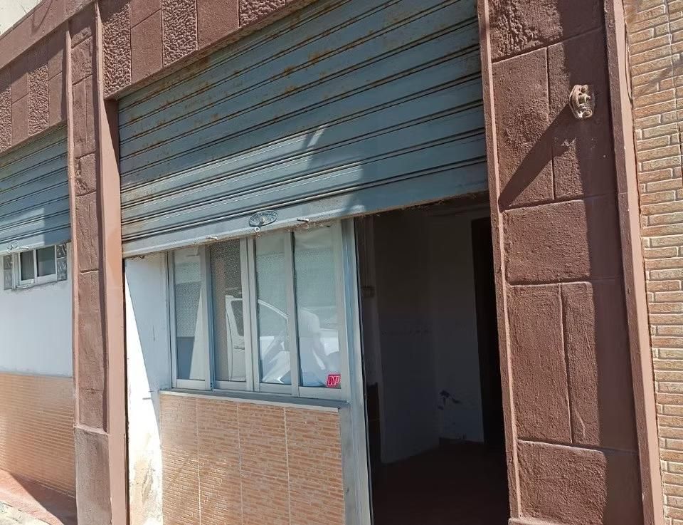 Escaparate con una persiana metálica azul parcialmente abierta y una ventana, visto desde el exterior bajo la luz del sol.